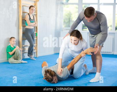 Beim Selbstverteidigungstraining vermittelt der Trainer Frauen die Technik, den Arm zu greifen und den Gegner auf den Boden zu senken Stockfoto