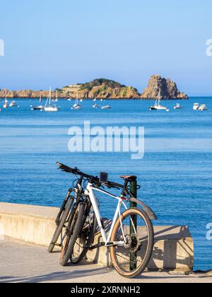 Cancale, Frankreich - 19. Juli 2024: Ruhige Küstenszene in Cancale, Bretagne, mit Fahrrädern, Meer, Booten, und Insel in der Ferne. Stockfoto