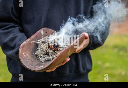 Menschliche Hände mit hölzerner Ritualschale und Feuer, Rauchzeremonie der australischen Aborigines, indigene Veranstaltung Stockfoto