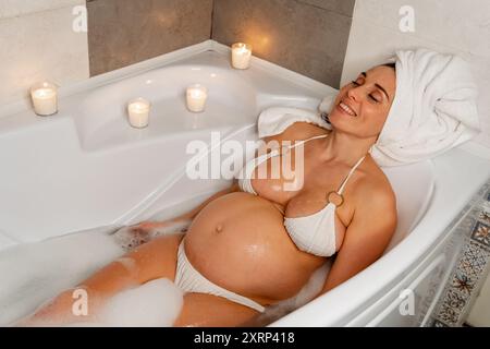 Werdende Mutter genießt ein Blasenbad mit Kerzen Stockfoto