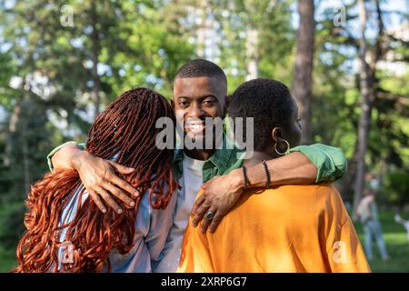 Ein lächelnder Afroamerikaner umarmt Freundinnen, die mit dem Rücken zur Kamera stehen. Freundschaft Stockfoto