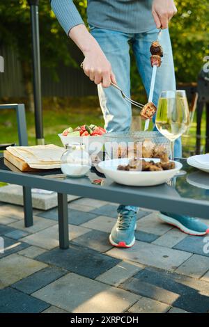 Ein nicht erkennbarer Mann entfernt Schweinefleischstücke, die auf dem Grill mit einer Gabel von einem Spieß gebraten wurden Stockfoto