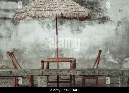 Ein strohgedeckter Regenschirm schattet eine Terrasse aus Bambus und Stein. Stockfoto