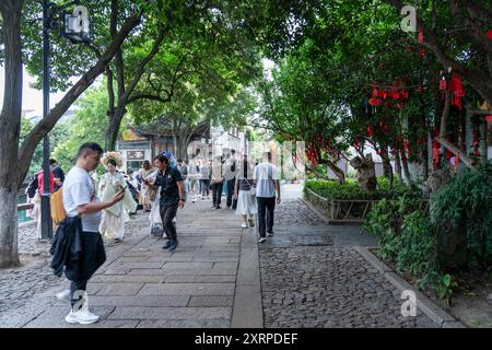 Suzhou, China - 11. Juni 2024 : Kopfsteinpflasterweg gesäumt von grünen Bäumen und roten Dekorationen in Suzhou, China. Stockfoto