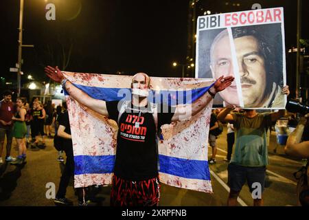 Tel Aviv, Israel. August 2024. Ein geknebelter Demonstrant mit gefälschtem Blut an den Händen und der israelischen Flagge. Er steht neben einem Plakat mit der Aufschrift „Bibi Escobar“ während der Demonstration. Tausende Israelis demonstrierten mit den Familien der Geiseln gegen Premierminister Benjamin Netanjahu und forderten einen sofortigen Geiselvertrag und Waffenstillstand - während Israel auf den Angriff der Iraner und der Hisbollah wartet. Quelle: SOPA Images Limited/Alamy Live News Stockfoto
