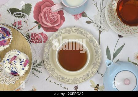 Tisch mit Blick von oben, dekoriert mit Retro-Servietten und rosa Tischdecke. Vintage-Teeparty um fünf Uhr. Teekanne, Milch, zwei Tassen Tee, Cupcakes. Stockfoto