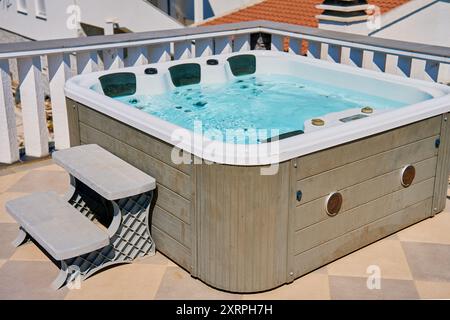 Whirlpool im Freien auf der sonnigen Dachterrasse mit sprudelndem Wasser und komfortablen Sitzgelegenheiten. Ort für Entspannung und Freizeit während des Sommerurlaubs Stockfoto