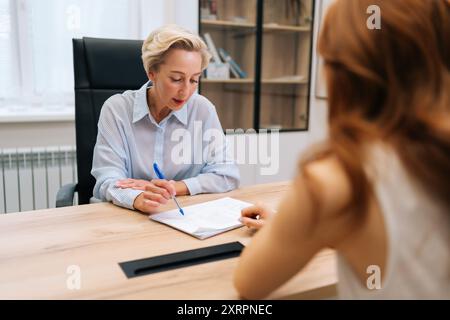 Mittelaufnahme einer freundlichen Ärztin mittleren Alters bei Beratung mit nicht erkennbarer Patientin. Lächelnder Praktizierender, der Profi gibt Stockfoto