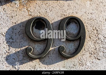 Nahaufnahme des Hausnummernschilds 99 an einer Wand. Hausnummer. Stockfoto