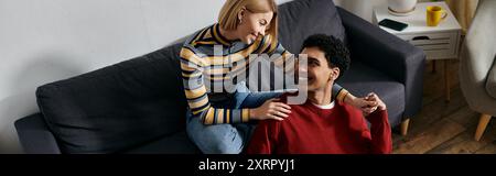 Ein glückliches, multikulturelles Paar entspannt sich auf einer Couch in ihrer modernen Wohnung und genießt die Gesellschaft. Stockfoto