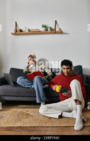 Ein glückliches multikulturelles Paar entspannt sich in einem modernen Apartment, genießt Kaffee und benutzt ihre Telefone. Stockfoto