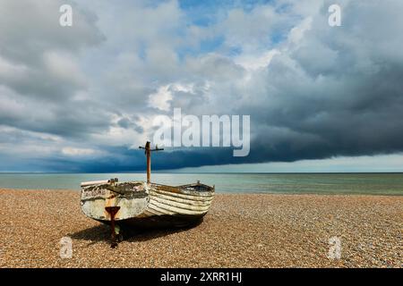 Verlassenes Fischerboot an einem Kieselstrand unter dramatischem bewölktem Himmel in der Nähe des Meeres Stockfoto