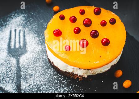 Ein Kuchen oder Dessert aus Mango- oder Sanddorngelee, überlagert mit Hüttenkäse-Creme und Schokoladenkeksen, dekoriert mit Preiselbeeren und Pulver Stockfoto