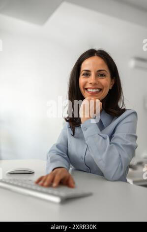 Porträt einer jungen, fröhlichen Frau, die an ihrem Schreibtisch sitzt Stockfoto