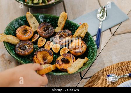 Die Hand greift nach sommerlich gegrilltem Brot und Pfirsichen auf Platte Stockfoto