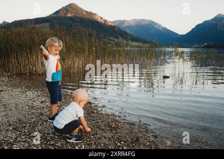 Entzückende kleine Kinder, die Steine in Wasser auf See an Bergen werfen Stockfoto