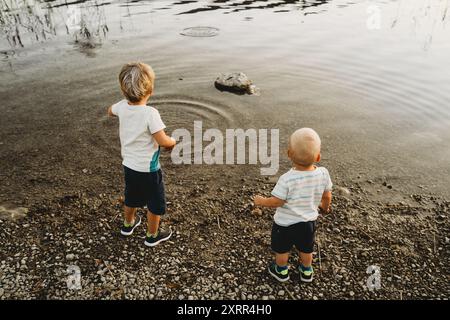 Weiße blonde Kinder spielen mit Steinen und Wasser am See Stockfoto