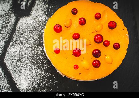 Ein Kuchen oder Dessert aus Mango- oder Sanddorngelee, überlagert mit Hüttenkäse-Creme und Schokoladenkeksen, dekoriert mit Preiselbeeren und Pulver Stockfoto