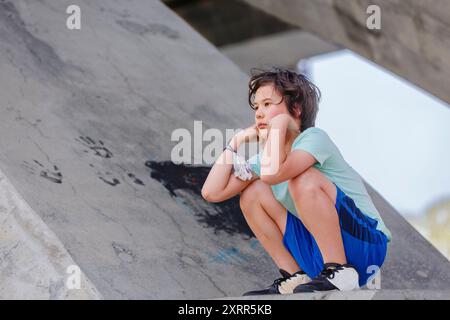 Ein nachdenklicher Junge sitzt allein auf einem großen Steinbau Stockfoto