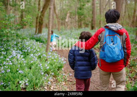 Vater geht Arm in Arm mit Kindern auf einem blumengesäumten Weg Stockfoto