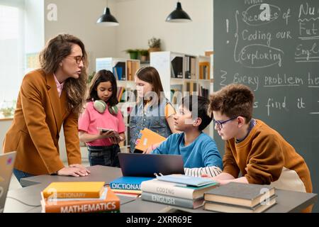 Lehrer, der mit einer Gruppe von Kindern spricht, die im Unterricht Computer verwendet Stockfoto