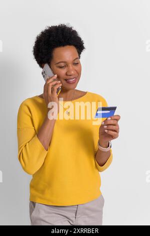 Junge Frau, die Kreditkartendaten teilt, während sie über das Mobiltelefon vor weißem Hintergrund spricht Stockfoto