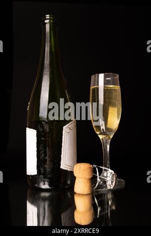 Eine Flasche Champagner mit einem vollen Glas, sprudelnd vor sprudelndem Wasser, und der Kork liegt in der Nähe. Alle werden vor schwarzem Hintergrund in vertikaler Fo angezeigt Stockfoto