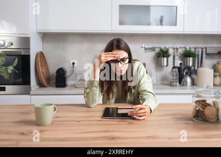 Junge verwirrte Frau mit Kreditkarte, die auf dem Bildschirm eines digitalen Tablets schaut, Probleme mit Online-Banking oder -Shopping, Kreditkartenlimit und Überspende hat Stockfoto