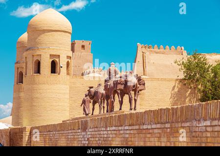 Skulpturengruppe einer Karawane mit Kamelen, die Güter entlang der Seidenstraße in der Nähe der alten Stadtmauern transportieren. Chiwa, Usbekistan - 17. Juli 2024. Stockfoto