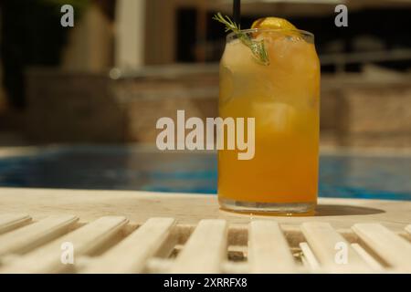 Ein Glas Limonade mit einer Zitronenscheibe auf der Oberseite sitzt auf einer Poolterrasse. Das Getränk wird in einem hohen Glas serviert, und die Zitronenscheibe verleiht einen erfrischenden Touch Stockfoto