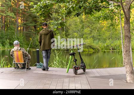 Zwei Männer fischen von einem hölzernen Dock an einem ruhigen Teich Stockfoto