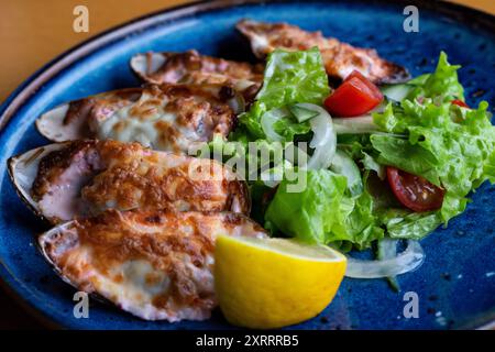 Fisch Und Meeresfrüchte. Muschelmuscheln. Gebackene Muscheln mit Käse, Koriander und Zitrone in Schalen auf gusseiserner schwarzer Platte. Teller mit Muscheln, kaltem Weißwein, Zitrone Stockfoto