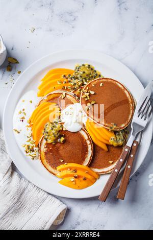 Frühstück Pfannkuchen mit Mango und Passionsfrucht auf weißem Teller, Blick von oben. Gesundes veganes Rezept. Stockfoto