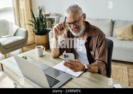 Ein reifer schwuler Mann mit grauen Haaren und Tattoos arbeitet von zu Hause aus. Stockfoto