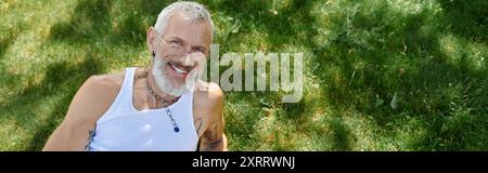 Ein reifer Schwuler mit Tattoos und grauem Bart lächelt im Freien. Stockfoto