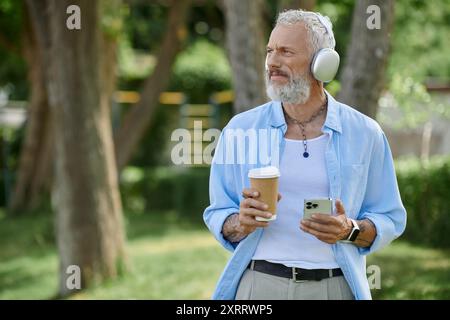 Ein reifer Mann mit Tattoos und grauem Bart, der eine Tasse Kaffee und Musik genießt Stockfoto