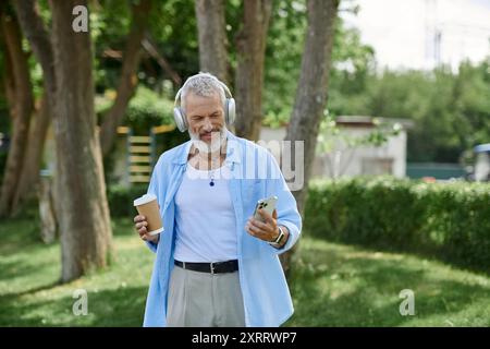 Ein Mann mit grauem Bart und Tattoos, der Musik lauscht und eine Tasse Kaffee genießt. Stockfoto