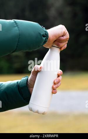 Der Mann hält eine Modell-Thermoskanne gegen verschwommene Büsche aus der Nähe Stockfoto