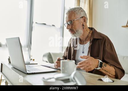 Ein reifer schwuler Mann mit Tattoos und grauen Haaren arbeitet fernab von seinem Home Office aus. Stockfoto