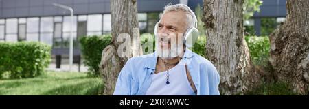 Ein Mann mit grauem Bart und Tätowierungen, der Musik mit anliegenden Kopfhörern hört. Stockfoto