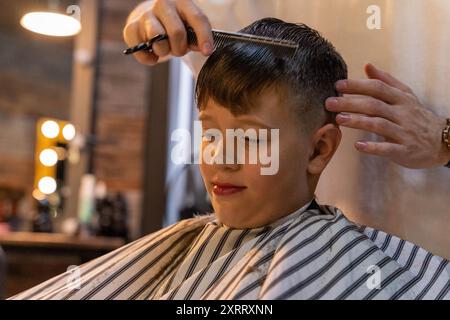 Ein kleiner Junge sitzt in einem Friseurstuhl und lässt sich die Haare schneiden. Stockfoto