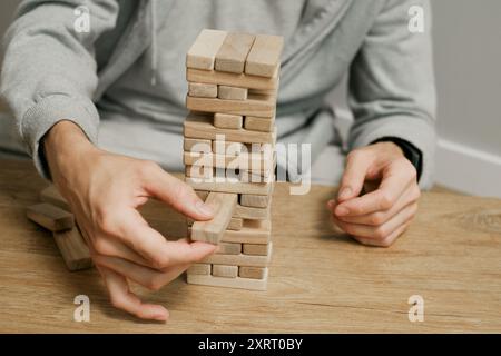 Person, die Holzblöcke stapelt, Turm baut, während sie an einem Tisch im Freien sitzt, konzentriert sich auf das Ausbalancieren der Teile. Nahaufnahme Stockfoto