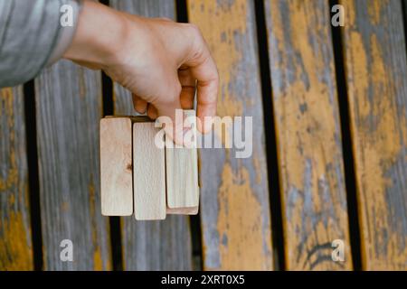 Person, die Holzblöcke stapelt, Turm baut, während sie an einem Tisch im Freien sitzt, konzentriert sich auf das Ausbalancieren der Teile. Nahaufnahme Stockfoto