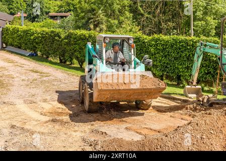 Ein Arbeiter auf einem Skin Loader bewegt Boden, der vor dem Haus ausgehoben wird. Aushubarbeiten und Außenpflaster. Stockfoto