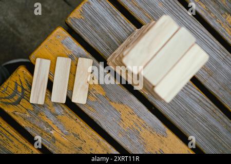 Person, die Holzblöcke stapelt, Turm baut, während sie an einem Tisch im Freien sitzt, konzentriert sich auf das Ausbalancieren der Teile. Nahaufnahme Stockfoto