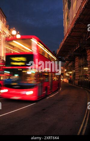 Roter Doppeldeckerbus, der in der Abenddämmerung durch die Straßen im Zentrum von London fährt. Stockfoto