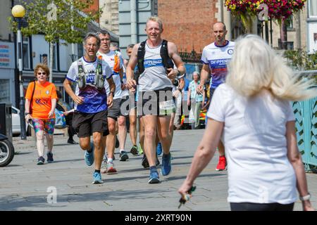 Chippenham, Wiltshire, Großbritannien. August 2024. Der 54-jährige Ultramarathonläufer Frank Wainwright (Mitte) läuft am 43. Tag seiner Englandreise durch seine Heimatstadt Chippenham. Er hat sich die Herausforderung gestellt, 62 Ultramarathons in 62 Tagen zu laufen, um Mittel für eine Reihe von Wohltätigkeitsorganisationen zu sammeln, darunter den Brathay Trust, der junge Menschen zu positiven Veränderungen inspirieren soll. Er machte sich am 1. Juli in Newcastle auf und wird seine Tour Ende August in Newcastle beenden. Quelle: Lynchpics/Alamy Live News Stockfoto