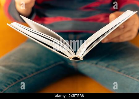 Ein kleiner Junge sitzt auf einer bequemen Couch, vertieft in ein Buch, sein neugieriger Ausdruck ist sichtbar, während er in die Geschichte eintaucht und ein gemütliches und einladendes schafft Stockfoto