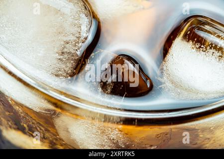 Hochwinkelansicht von Eiswürfeln, die im durchlüfteten Cola-Wasser in transparentem Glas schweben, Nahaufnahme. Stockfoto