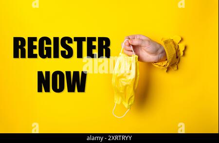 Eine Hand, die eine gelbe Maske hält und darunter die Worte Registrieren steht. Begriff der Dringlichkeit und Wichtigkeit, da die Person eine Maske hält, die ich Stockfoto